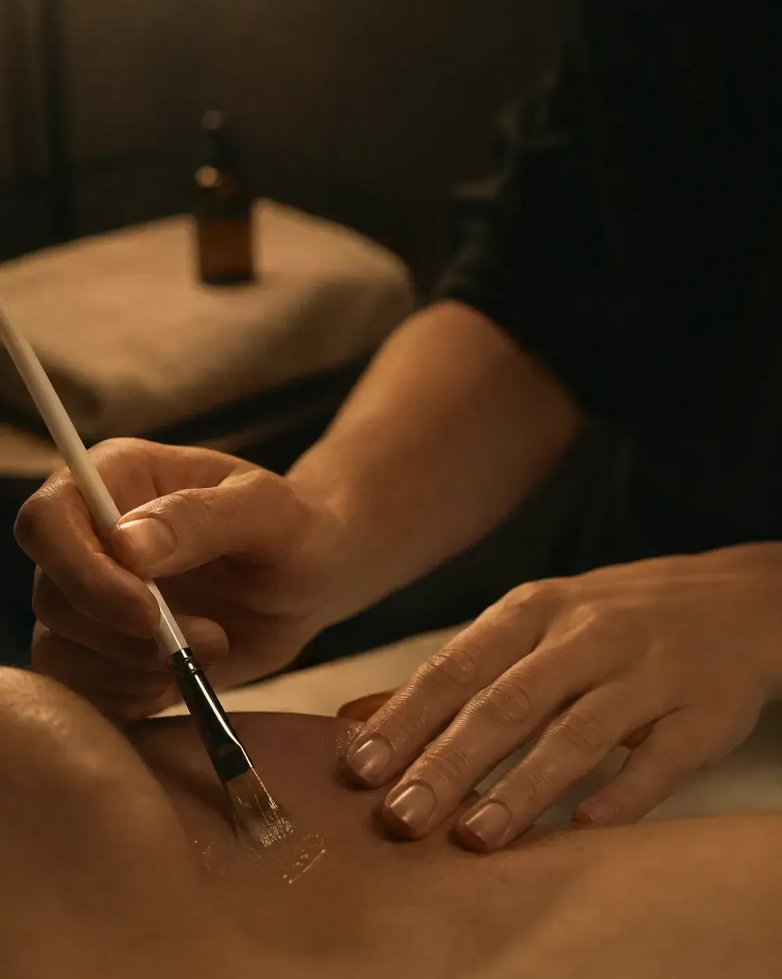 A close crop of hands during a cosmetic treatment, lit in the same warm tones as the hero still-life.